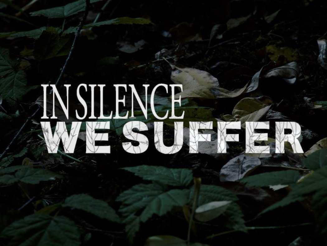 Title logo for IN SILENCE WE SUFFER, our short film from 2019. The text is laid over a darkened photo of a forest floor. The IN SILENCE text is a thin, sleek font, while the WE SUFFER is in a bold font that looks encroached in veins or vines.